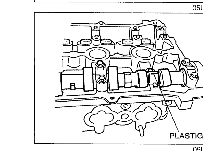 Plastigage strips placed atop the camshaft journals on the cylinder head along the axial direction for camshaft oil clearance measurement. Label 'PLASTIGAGE' identifies the strips.