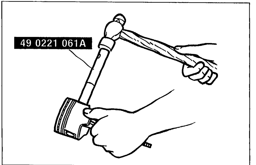 Hand using SST 49 0221 061A (piston pin installer) to tap a piston pin into the piston/connecting rod assembly. The piston is gripped and supported while the SST drives the pin.