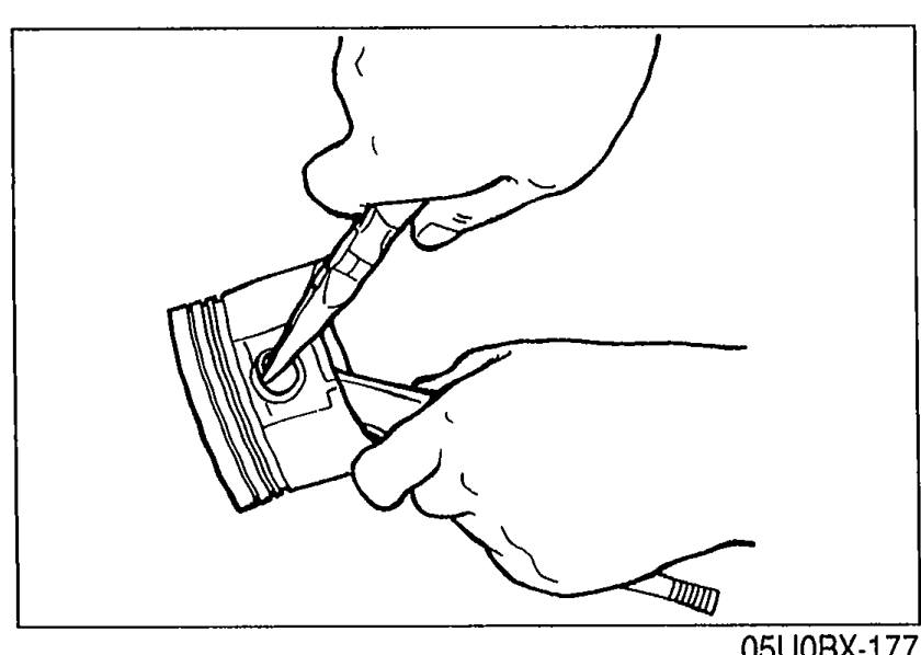 Hands using a pick/tool to install the second piston pin clip into the clip groove on the piston.