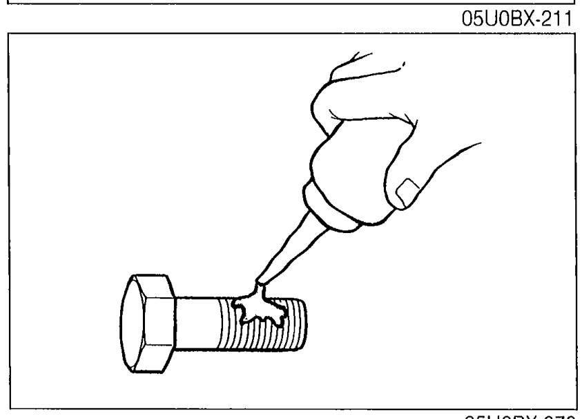 A hand applying sealant from a tube to the threads of a flywheel bolt.
