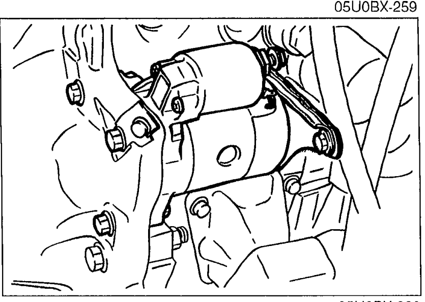 Close-up of the starter motor installed at the transmission housing, showing the mounting bolts.