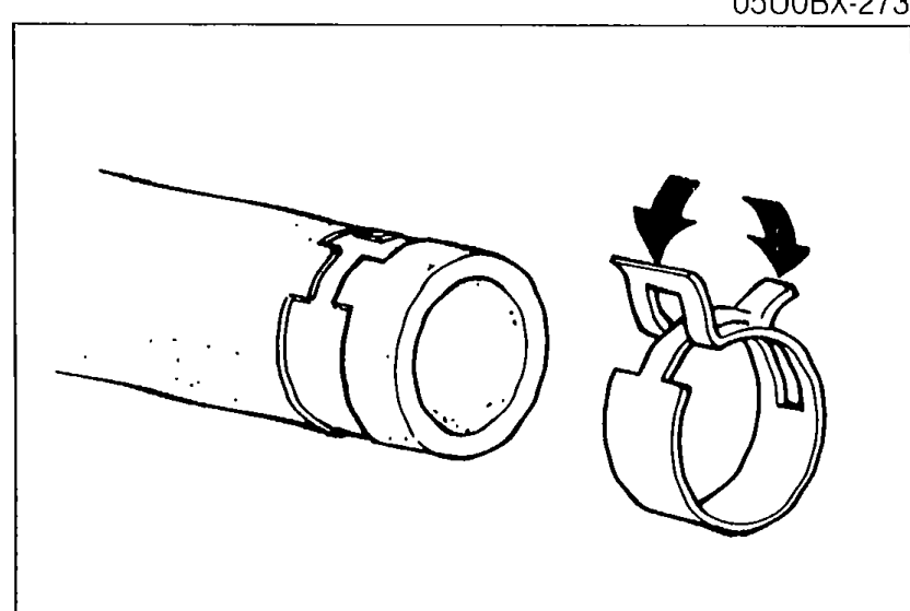 Close-up of a hose clamp on a radiator hose with two arrows pointing inward, illustrating the clamp-squeeze action described in the caution.