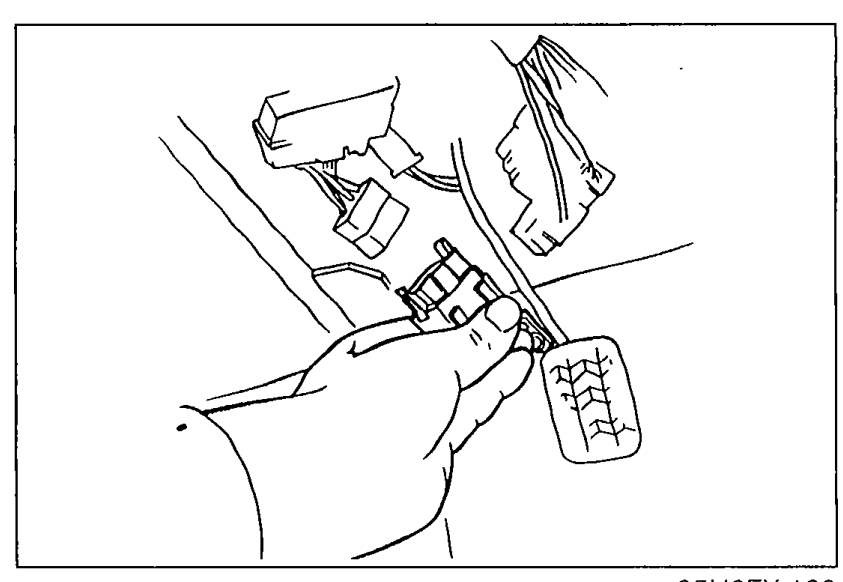 Photo of a hand disconnecting the fuel pump connector to release fuel system pressure before performing pressure regulator inspection.