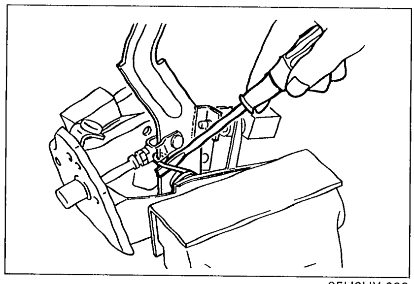 Photo of the clutch pedal assembly held in a vise, technician using pliers to pry the return spring off the clutch pedal during removal.