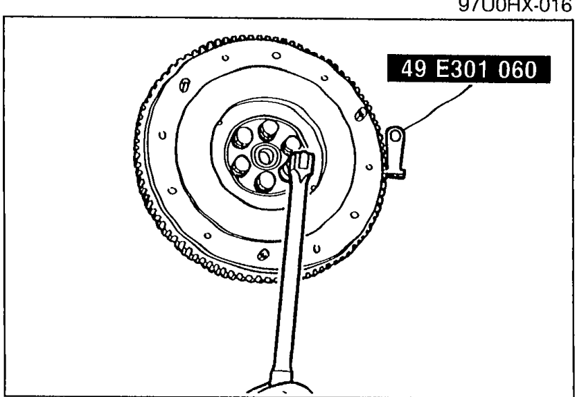 Photo of the flywheel with SST 49 E301 060 engaged on the ring gear to hold the flywheel while removing its bolts.