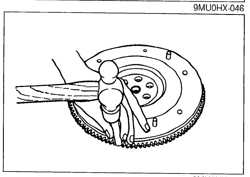 Removing the ring gear from the flywheel: pliers/tool prying the heated ring gear off after applying a blowtorch around its circumference.