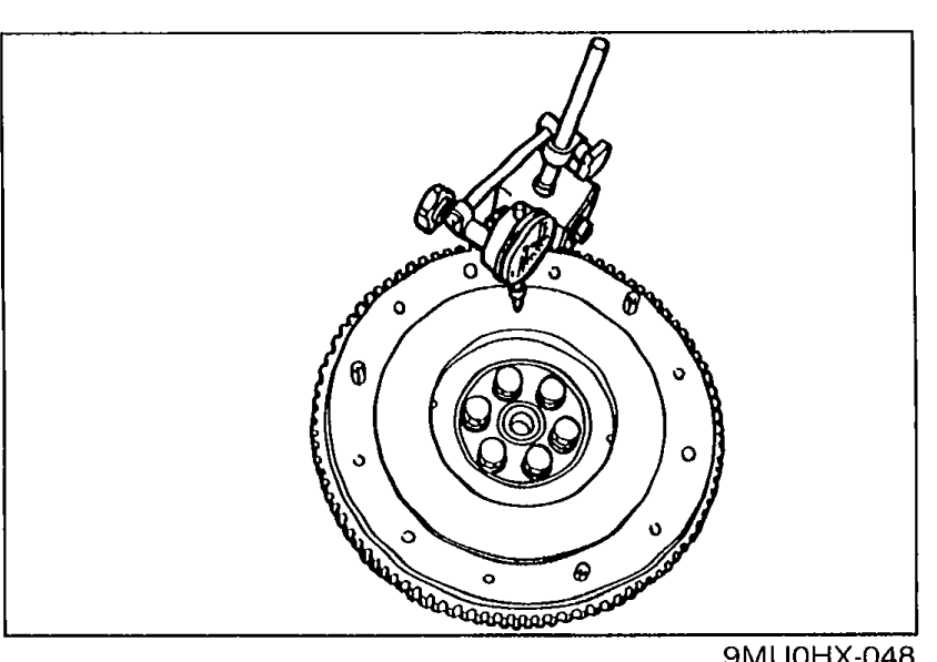 Flywheel mounted with a dial indicator measuring runout on the clutch friction face. Shows the dial indicator stand contacting the flywheel friction surface.