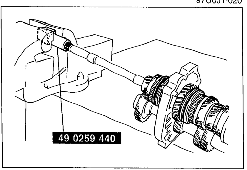Mainshaft clamped in vise using SST 49 0259 440. Hands operate the SST to hold the mainshaft for locknut removal.