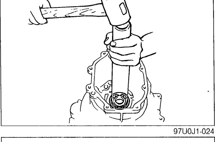 Mainshaft assembly held vertically in a vise with copper hammer being applied — illustrates securing the bearing housing in vise and removing the locknut.