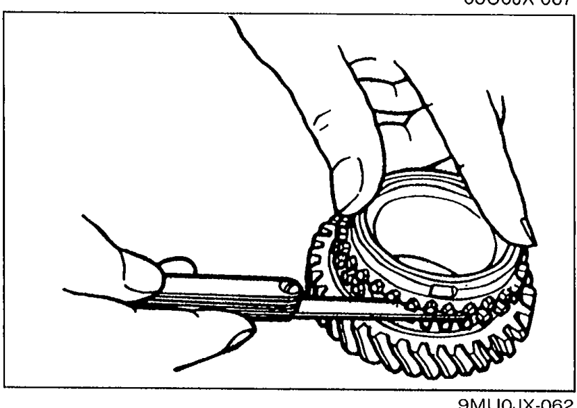 Hands using a feeler gauge to measure the clearance between the synchronizer ring and the flank surface of the gear, with the synchronizer ring seated squarely on the gear.