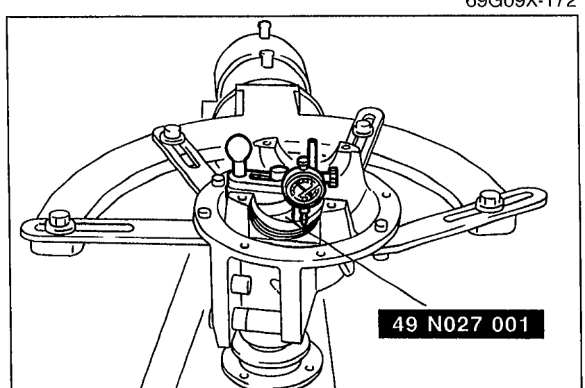 Illustration showing SST 49 N027 001 placed atop the drive pinion model with the gauge body atop the gauge block, and the dial indicator feeler measuring at the bearing inner race (side bearing) seat positions on the left and right.