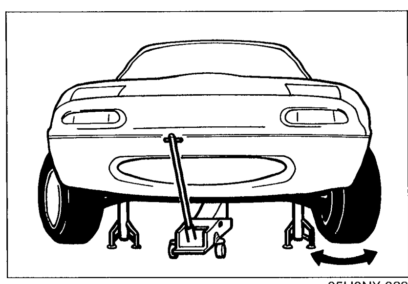 Rear-three-quarter view of an MX-5 raised on a floor jack with both front wheels off the ground, ready for steering wheel exercise during air bleeding.