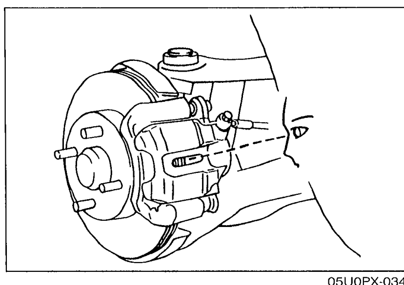 Photograph of the front disc brake assembly with the wheel removed, showing the caliper, rotor, and inspection hole through which the pad thickness is sighted during quick inspection.
