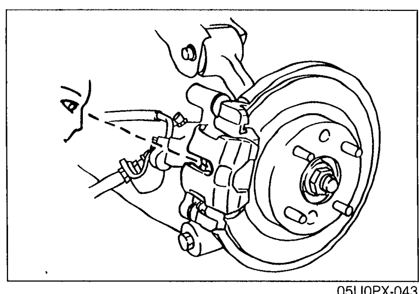 Illustration of the rear disc brake assembly with the wheel removed, showing the caliper and rotor; the technician sights through the caliper inspection hole (arrow) to gauge remaining pad thickness.