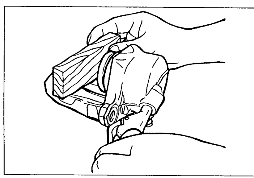 Illustration showing a piece of wood placed in the caliper and compressed air being blown through a hole to force the piston out of the caliper.