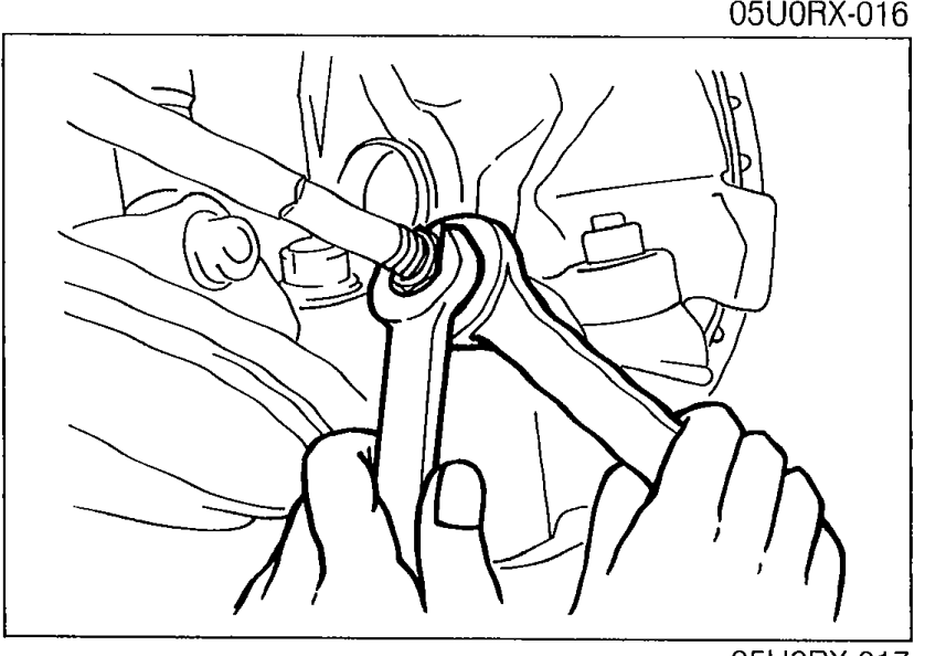 Photo showing a hand using a wrench on the tie-rod with the steering gear boot visible; illustrates tie-rod adjustment for toe-in.