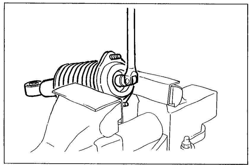 Shock absorber held in a vise; piston rod upper nut being loosened a few turns with a wrench/socket.
