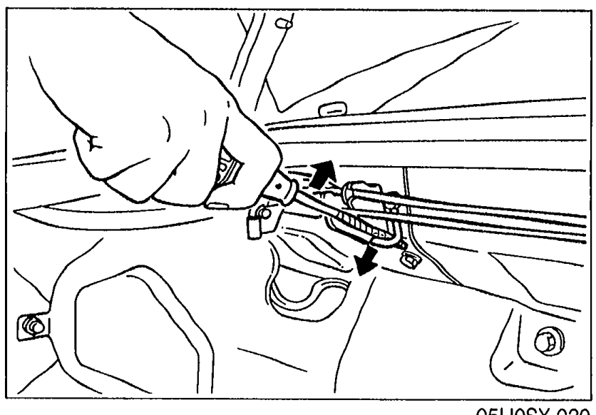 Photo showing a hand using a protected screwdriver to lift the trunk balance spring out of its mount. Illustrates the removal step for the balance spring.