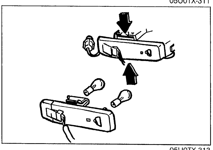 Back-up light bulb assembly being removed/replaced; shows the lamp housing with a bulb partially extracted and an arrow indicating the removal direction.