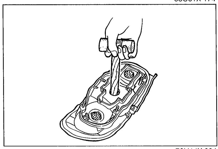 Rear combination light assembly with a hammer handle / round bar being pushed against the rear of the lens to separate it from the housing (Step 2).