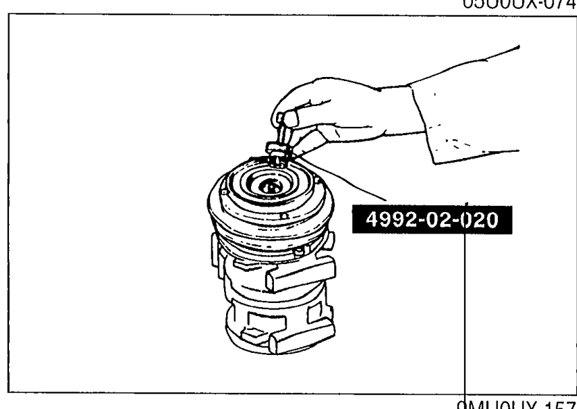 Technician using SST 4992-02-020 (pressure-plate puller) threaded into the clutch hub to extract the pressure plate from the compressor.