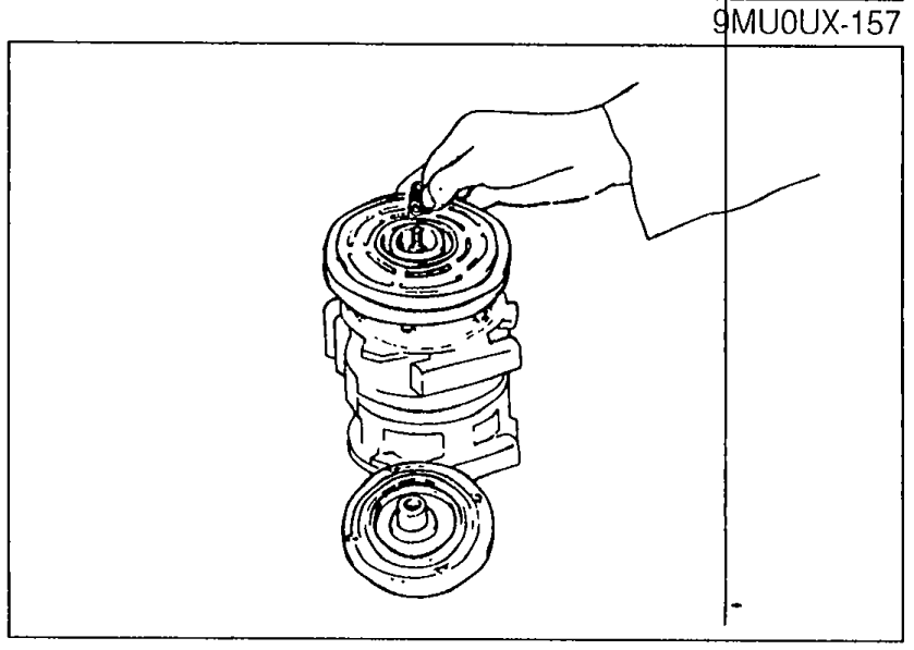 Removing the shims from the compressor shaft after the pressure plate is off; hand shown lifting the shim stack with the rotor still in place.