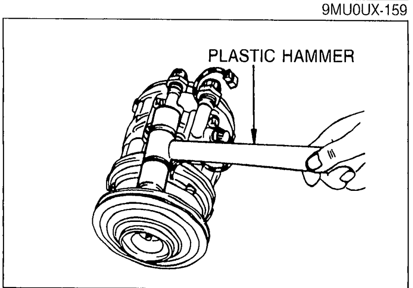 Using a plastic hammer to lightly tap the rotor off the compressor shaft. The pulley is visible adjacent to the rotor and must not be damaged during this operation.