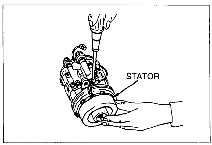 Hand disconnecting the stator wires from the compressor housing; the stator coil is visible inside the compressor body.